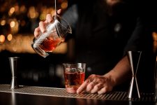 bartender pours drink into cocktail with ice